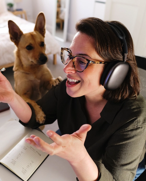 woman smiling working at dekstop with a dog by their side